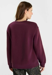 Purple sweatshirt with a relaxed fit, crew neckline, and ribbed cuffs. Textured fabric and dropped shoulders. Paired with leopard print pants.