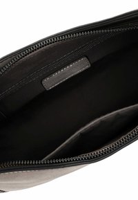 Interno di una borsa nera con zip, foderato in grigio; materiale liscio, una tasca interna e un'etichetta. Design minimalista, layout spazioso.