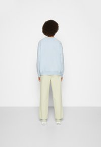 Suéter azul claro con escote redondo, mangas raglán y puños. Combinado con pantalones amplios amarillos claros. Diseño simple y corte relajado.