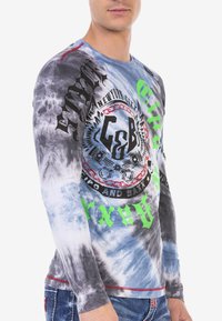Langarmshirt in Batik-Tönen von Schwarz, Blau und Weiß. Mit grafischem Druck in Rot- und Grüntönen und strukturiertem Stoff.