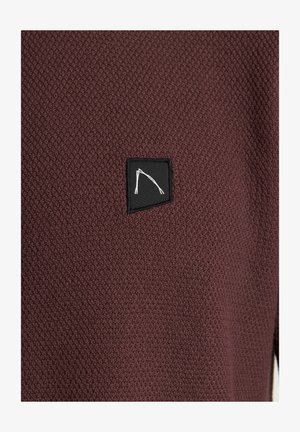 Burgundsko teksturirano platno z majhnim črnim madežem, ki ima belo obriso obliko gore, postavljeno na levi strani.