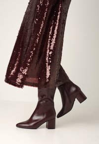 Burgundské ankle boty s špičatou špičkou a blokovým podpatkem, vyrobené z hladké kůže, spárované s burgundskou sukní zdobenou flitry.
