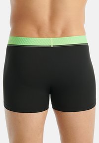 Svarta badshorts med en texturerad grön midjeband. Midjebandet har en kontrasterande svart rand längs den övre kanten.