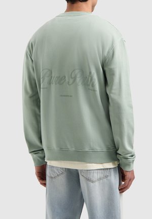 Mint green sweatshirt with ribbed cuffs and hem, featuring embossed "Pure Path" text on the back. Soft fabric. Worn over a light shirt.