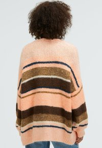 Knitted oversized sweater in peach with horizontal stripes in brown, cream, and navy. Features a soft texture and a relaxed fit.