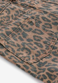 Tissu beige avec motif léopard noir, montrant une poche cousue et des détails de coutures sur un vêtement.
