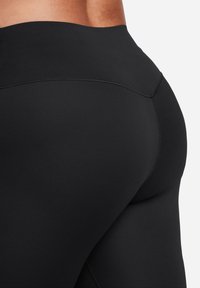 Sorte leggings laget av glatt, elastisk materiale. Høy midje med flate sømmer og en støttende passform som fremhever den naturlige kurven.