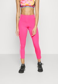Skräddarsydda rosa leggings med vita sidstrimmor, stretchigt material och kort längd, kombinerat med en färgglad sportbh och svarta sneakers.