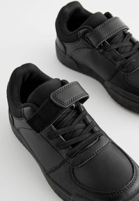 Baskets noires en cuir et tissu, avec une sangle en velcro, des lacets, un col rembourré et des semelles en caoutchouc texturé.