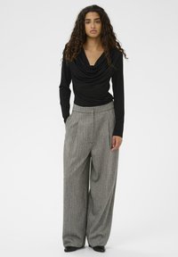 Melna garām piedurknēm blūze ar atspiedienu kakla izgriezumu, apvienota ar augsto jostu pelēkajām platajām biksēm ar rakstu un melnām kurpēm.