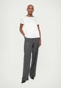 Biała bluzka z krótkim rękawem i okrągłym dekoltem, zestawiona z dopasowanymi szarymi spodniami. Strój charakteryzuje się czystymi liniami i luźnym krojem.