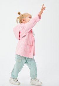 Chaqueta con capucha de color rosa claro con dos bolsillos frontales, combinada con pantalones de quilt de color verde menta que tienen un bolsillo lateral. Modelo lleva zapatillas blancas.