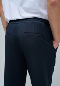Pantalones deportivos de color navy con cintura elástica, que cuentan con dos bolsillos traseros y una textura de tela suave y ligera.