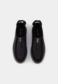 Paire de chaussures noires à enfiler avec fermetures éclair à l'avant, languettes à l'arrière et semelles en caoutchouc texturées, vues de dessus sur fond blanc.