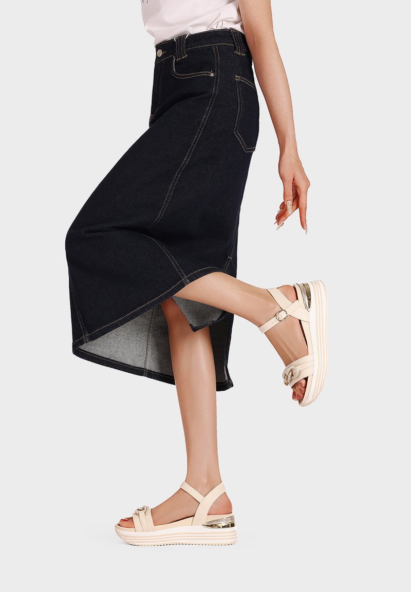 Gonna midi in denim scuro con orlo asimmetrico, abbinata a sandali platform beige con cinturini regolabili e dettagli metallici.