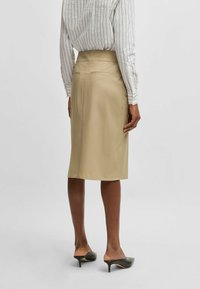 Beige knee-length skirt in a smooth fabric with a fitted waist and concealed back zipper, paired with black open-toe heels.