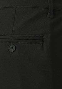 Nadclose slika crnih platnenih hlača s stražnjim džepom s preklopom, učvršćenim crnom tipkom i detaljem u obliku remenice.