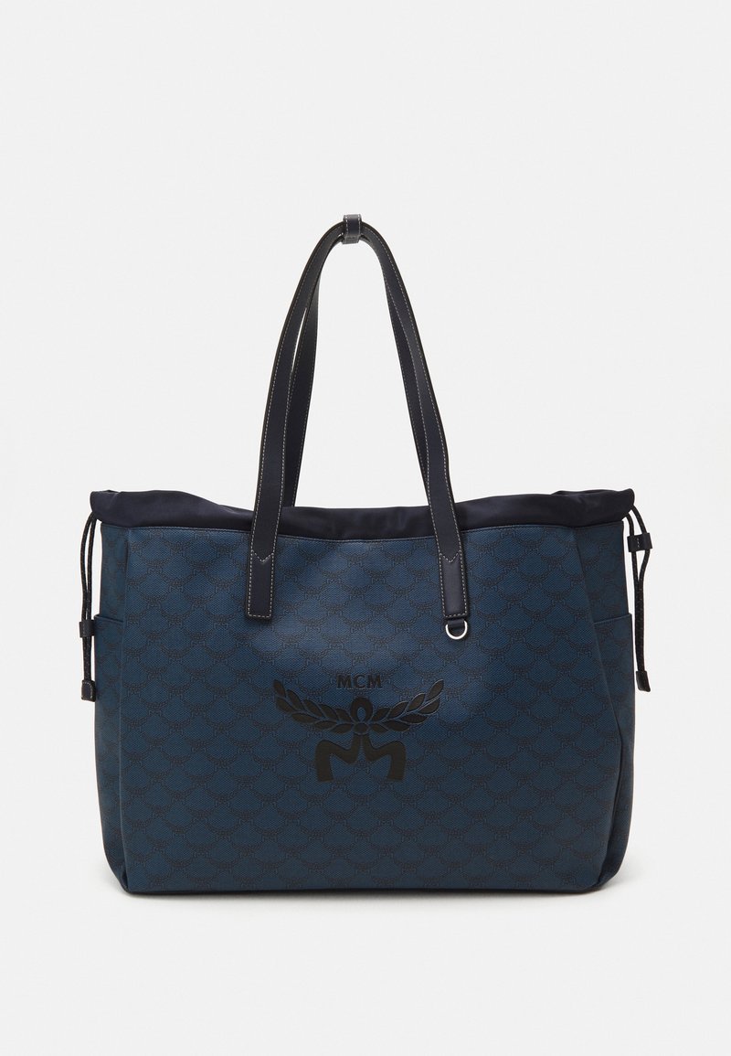 Sac fourre-tout bleu en matériau texturé avec un dessus à cordon, présentant un design de logo noir et des poignées en cuir noir.