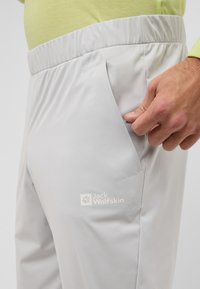 Hellgraue, elastische Hose mit seitlichen Taschen. Sie verfügt über ein dezentes Logo und eine glatte Textur, die für Komfort und Beweglichkeit sorgt.