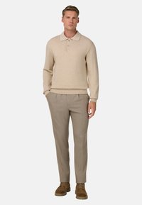 Beige neulepikeepaita, jossa kaulus ja kaksi nappia, yhdistetty vaaleanruskeisiin räätälöityihin housuihin ja ruskeisiin mokkanahkakenkiin.