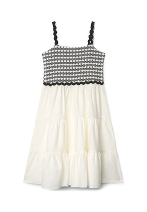 Robe blanche sans manches avec jupe à volants, corsage à motifs noirs et blancs, et bretelles ainsi que bordure à la taille en dentelle noire.