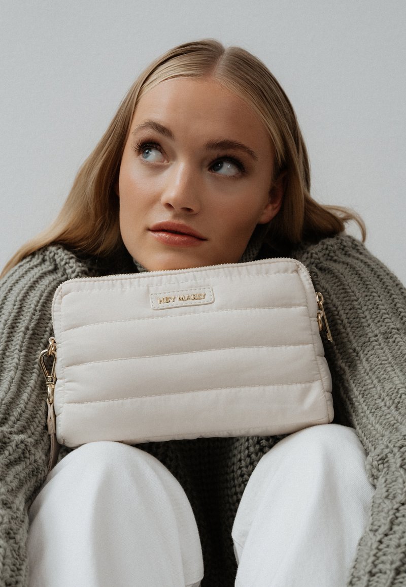 Licht beige gestikte pouch tas met een gouden rits en hardware. Zachte textuur, rechthoekige vorm, met een subtiele merkl logo.