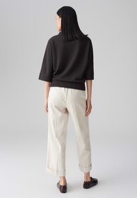 Top noir texturé à manches trois-quarts, associé à un pantalon large crème et des chaussures slip-on marron foncé.