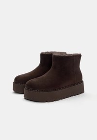 Stivali ankle in suede marrone con fodera in morbido pelliccia, suola piattaform spessa e cuciture decorative lungo il bordo.
