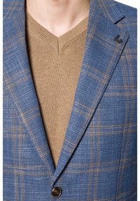 Niebieska marynarka w kratę z brązowymi akcentami, fakturowana tkanina, klapy wykładane, a pod spodem brązowy sweter w serek. Widoczne detale guzików.