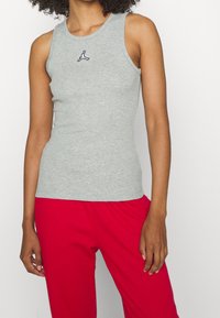 Gray sleeveless tank top with a round neckline and a small black logo on the chest, paired with red loose-fit pants.