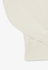 Manica di un maglione lavorato a maglia color crema con un polsino a coste. La texture morbida e il design snello enfatizzano la semplicità e la funzionalità.
