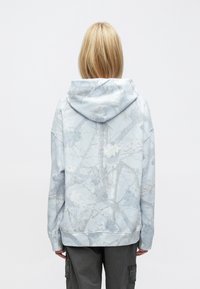 Világoskék kapucnis pulóver szürke árnyalatú ágmintával, laza fazonban, bordázott szegéllyel a szegélyén.