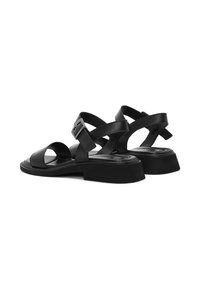 Sandalias de cuero negro con tacón cuadrado, punta abierta, tiras cruzadas y cierre de hebilla ajustable. Textura suave con detalles mínimos.