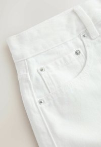 Gros plan sur un jean en denim blanc montrant la ceinture, la poche avant, la petite poche à monnaie et les rivets argentés.