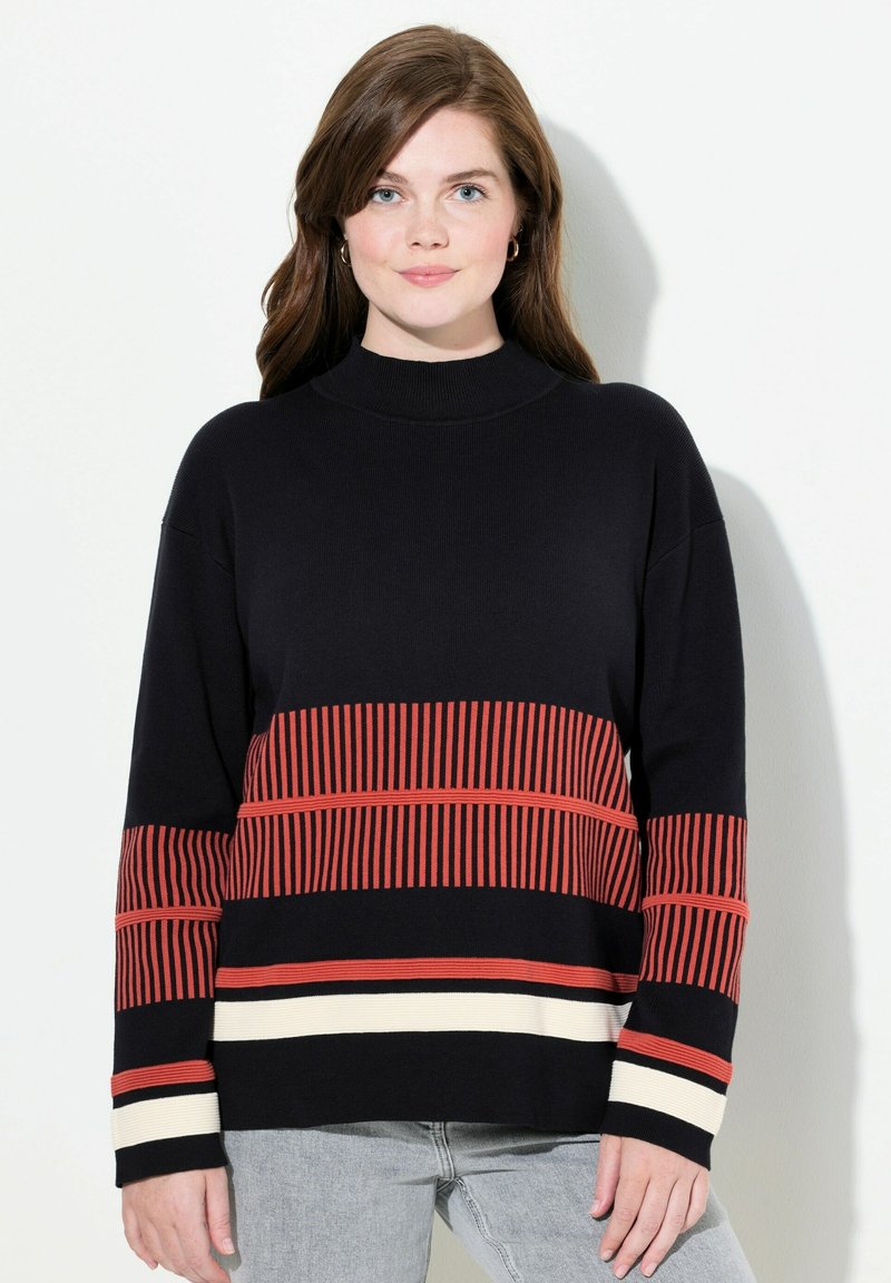 Schwarzer Strickpullover mit hohem Kragen, der horizontale rote und cremefarbene Streifen aufweist, sowie langen Ärmeln mit gestreiften Akzenten an den Bündchen.