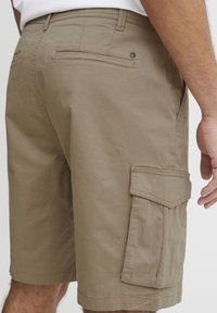 Kaki színű cargo rövidnadrág sima pamut keverékből, oldalsó zsebbel, két hátsó zsebbel és diszkrét varrási részletekkel.