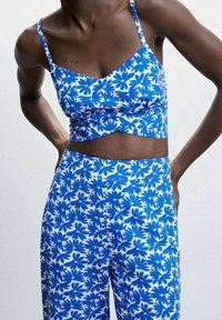 Květinový top na ramínka v modro-bílé barvě s crop střihem, doplněný širokými kalhotami ve stejném designu. Měkká látka s hladkým povrchem.