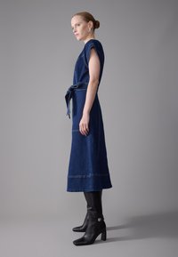 Denim dress with short sleeves, belted waist, and straight silhouette, in dark blue; paired with black square-toed ankle boots.