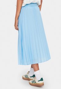 Pleated midi-hame vaaleansinisessä värissä, jossa on elastinen vyötärö ja virtaava kangas pehmeällä tekstuurilla. Yhdistetty valkoisiin sukkiin ja rentoihin tennareihin.