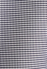Tessuto blu navy e bianco caratterizzato da un motivo geometrico a houndstooth, con una superficie testurizzata e una struttura a tessitura stretta.