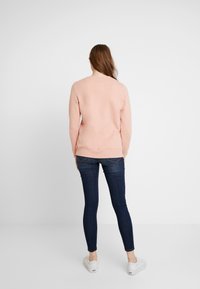 Rosa sweatshirt med ribbad mudd och nederkant, tillsammans med slim-fit mörk denimjeans och vita sneakers, sedd bakifrån.