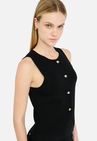 Black sleeveless top featuring a fitted design, knit texture, and five metallic buttons along the front. Side cutouts enhance ventilation.