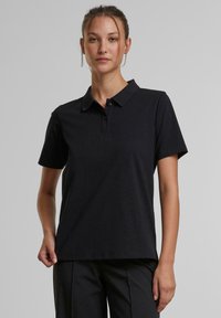 Černé polo tričko s krátkými rukávy, klasickým límečkem a třemi knoflíky u výstřihu. Vyrobeno z jemné, texturované tkaniny.