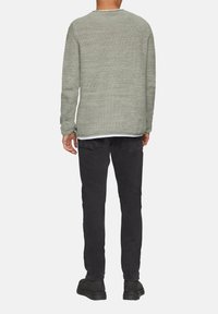 Grauer gestrickter Pullover mit strukturiertem Muster, Rundhalsausschnitt, kombiniert mit schwarzen Slim-Fit-Jeans und schwarzen Schuhen, von hinten betrachtet.