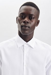 Witte overhemdd met een klassieke kraag, gemaakt van gladde stof. Beschikt over een gestructureerde pasvorm en subtiele glans. Geen zichtbare patronen of accenten.