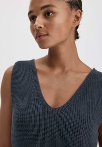 Navyblauw gebreide tanktop met een diepe V-hals en een geplisseerd patroon. Mouwloos ontwerp dat een gladde halslijn en een figuurvolgend pasvorm toont.