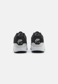 Les baskets Nike Air noires et grises présentent un dessus texturé, des accents en cuir lisse, une semelle intermédiaire épaisse blanche et une semelle extérieure en caoutchouc noir.