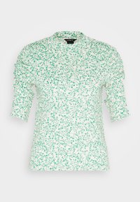 Blouse blanche à manches courtes avec imprimé délicat de vignes et feuilles vertes, détails froncés sur les manches, encolure ronde, et étiquette Lindex à l'intérieur du col.
