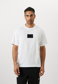 Witte katoenen t-shirt met een zwart rechthoekig Nike-logo op de borst. Heeft korte mouwen en een ronde hals.