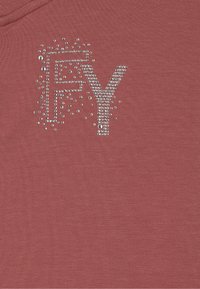 Sudadera de color rosa decorada con las letras "FY" adornadas con strass transparentes, sobre un fondo de tela texturizada.